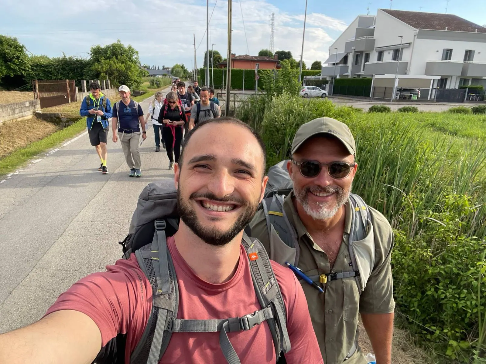Due coach in testa a un gruppo in cammino, zaino in spalla, su una strada di campagna