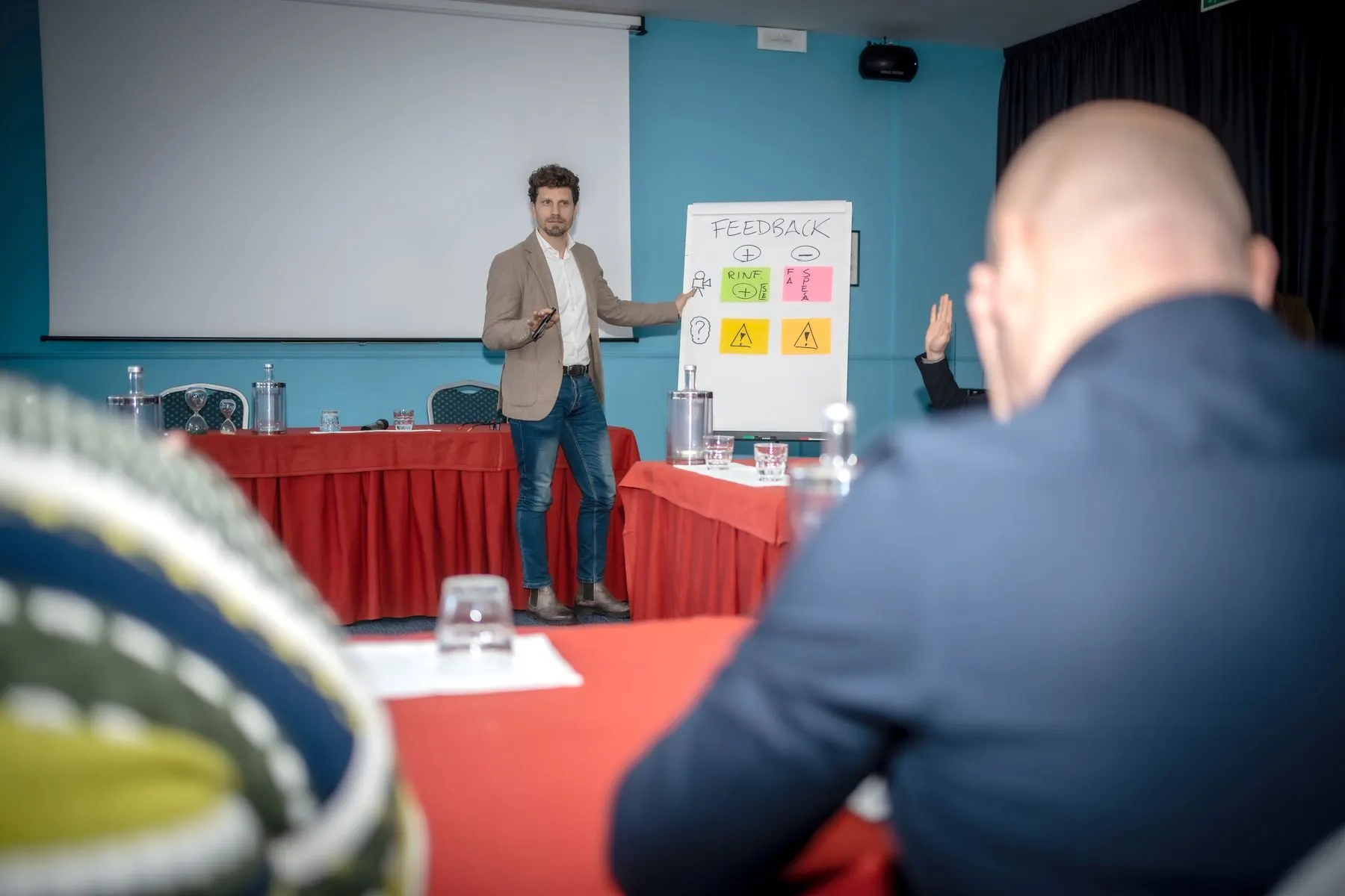 Un docente spiega al flipchart davanti a un'aula, ripreso da dietro i partecipanti